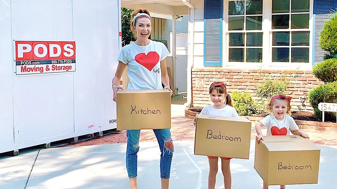 A family poses in front of a PODS container while holding moving boxes