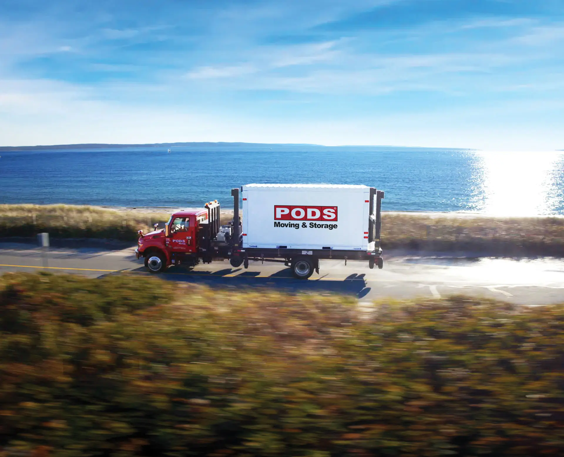 A PODS moving truck driving on a seaside road