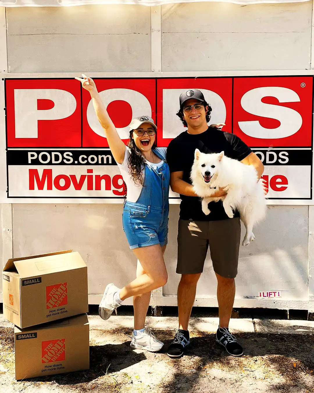 Two PODS customers pose in front of a PODS container while holding their dog