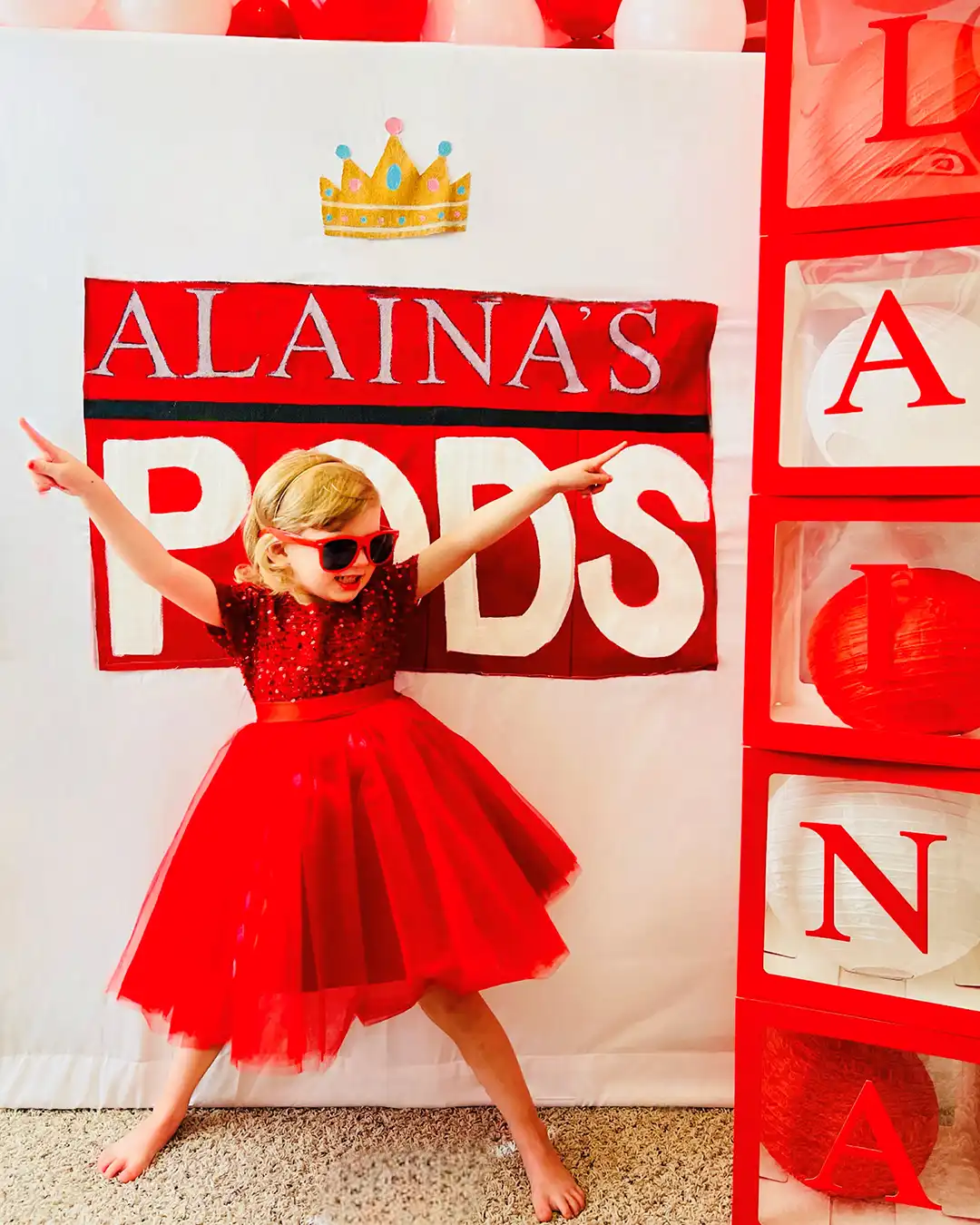 A child wearing sunglasses poses in front of a homemade PODS banner