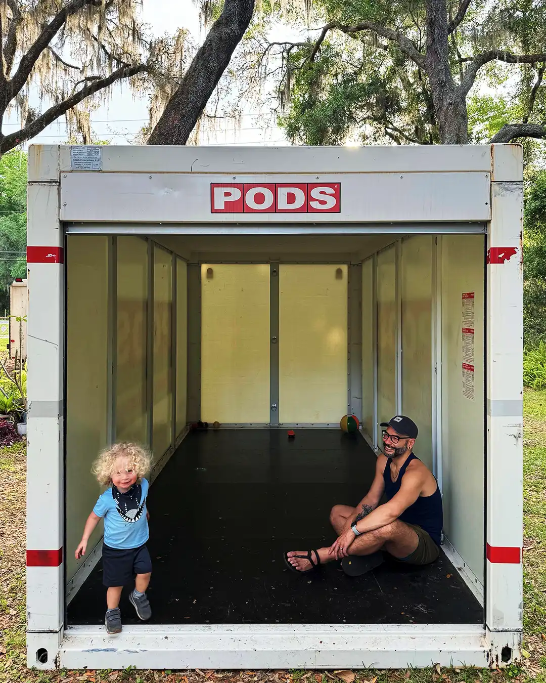 A father and child play inside of an empty PODS container